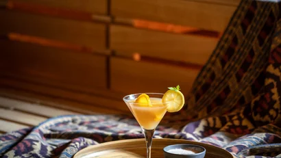 Cocktailglas mit Orangen- und Zitronenscheibe auf Holztablett im gemütlichen Raum