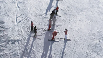 Mehrere Skifahrer auf verschneitem Hang mit langen Schatten im Sonnenlicht