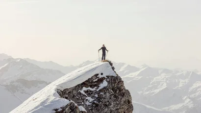Person steht auf schneebedecktem Berggipfel mit Blick auf Berge