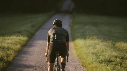 Radfahrer mit Kamera auf dem Rücken auf einem Landweg bei Sonnenlicht