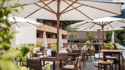 Terrasse mit Holzstühlen und großen weißen Sonnenschirmen bei sonnigem Wetter