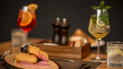 Gebackene Häppchen mit rosa Sauce auf Holzbrett und Getränke im Hintergrund