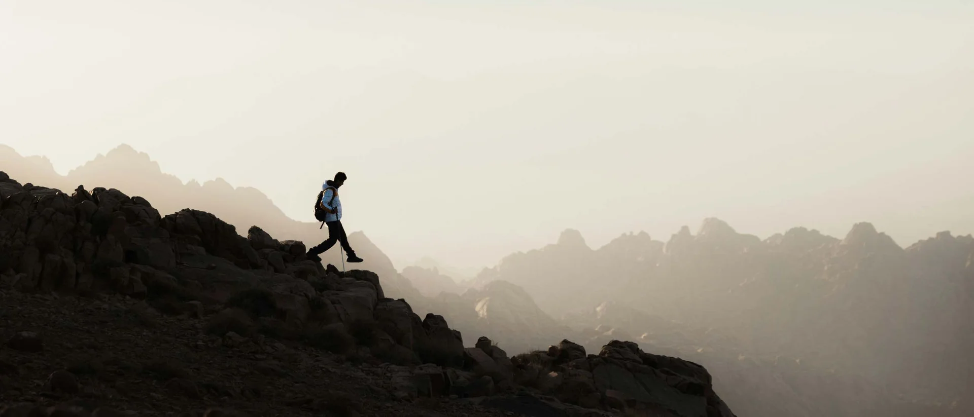 Wanderer läuft bergab bei bewölktem Himmel und bergiger Landschaft