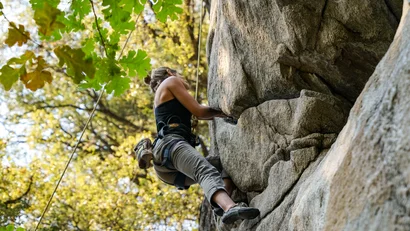 Person beim Klettern an einer Felswand im Wald