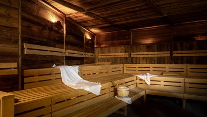 Innenraum einer warm beleuchteten Holzsauna mit Handtüchern und Saunaeimer