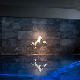 Beleuchtetes Berglogo an dunkler Wand über blau leuchtendem Pool
