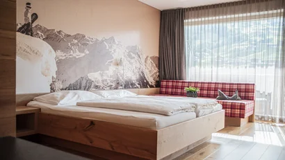 Schlafzimmer mit Doppelbett, Bergwandbild und kariertem Sofa vor Fenster
