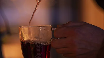 Hot drink being poured from ladle into glass with steam rising
