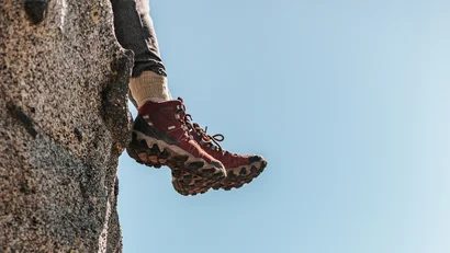 Wanderschuhe hängen über einer Felskante mit Berglandschaft im Hintergrund