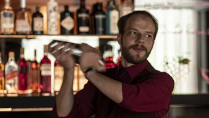 Barkeeper schüttelt Cocktailshaker hinter gut ausgestatteter Bar
