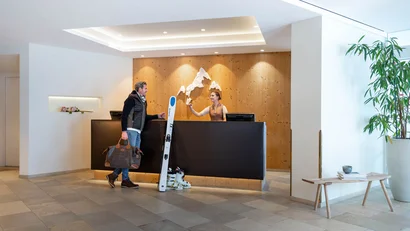 Gäste checken in der Hotellobby mit Ski-Ausrüstung ein