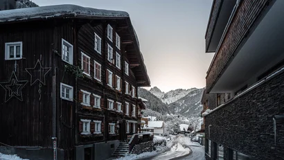 Verschneite Straße zwischen Holzhäusern im Bergdorf bei Sonnenuntergang