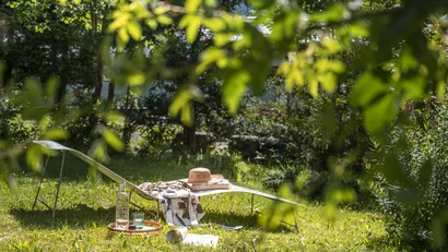 Liegestuhl mit Hut und Getränken in sonnigem Garten