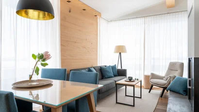 Moderner Wohnraum mit blauem Sofa, Stühlen und Stehlampe vor großen Fenstern