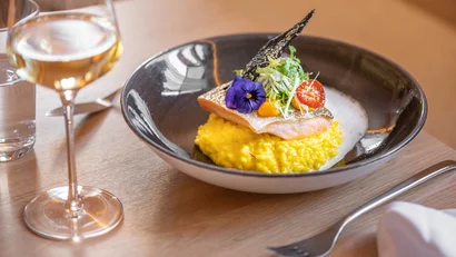 Lachs auf Safranrisotto mit Gemüse und Blume in schwarzer Schüssel