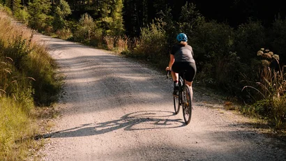 Fahrradfahrer auf Waldweg mit Bergen im Hintergrund