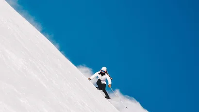 Skifahrer fährt einen steilen Hang bei klarem Himmel hinunter