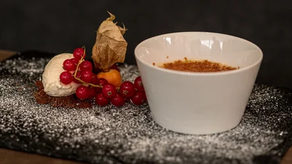 Crème Brûlée Dessert mit Beeren und Sahne auf schwarzem Teller