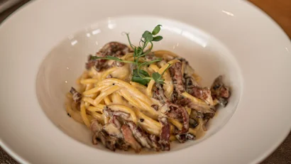 Teller mit cremiger Pasta und Rotweinglas auf Holztisch