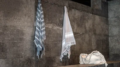 Zwei Handtücher hängen an Haken über einer Steinbank in einem grauen Raum