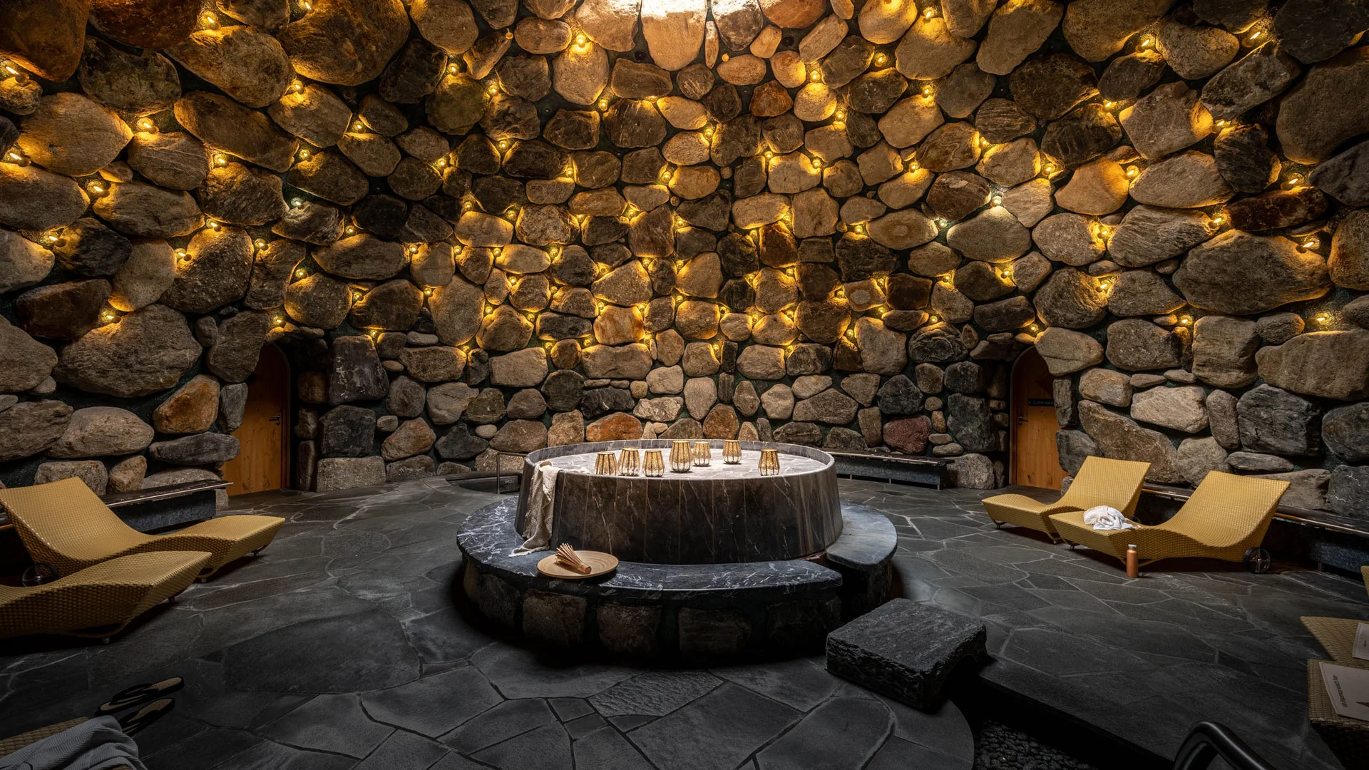 Runde Steinhöhle mit warmen Lichtern und zentralem Marmortisch
