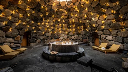 Runde Steinhöhle mit warmen Lichtern und zentralem Marmortisch